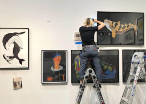 Art Work FAS team member drills screws in the wall for art installation project.